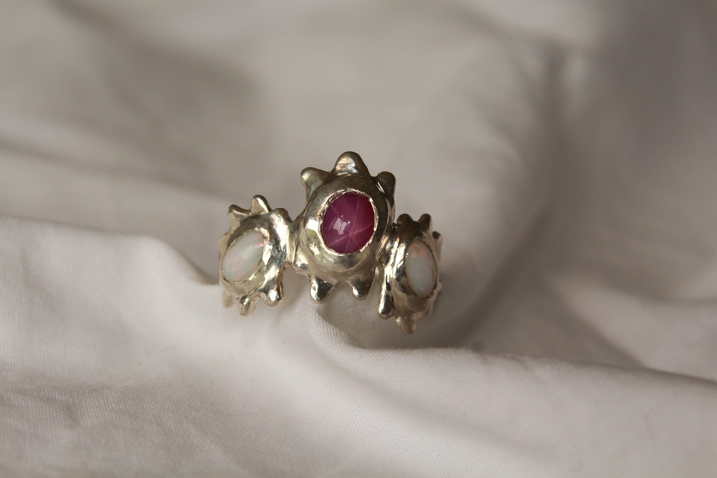 Silver ring with a large ruby and opal gemstones, placed on white fabric.