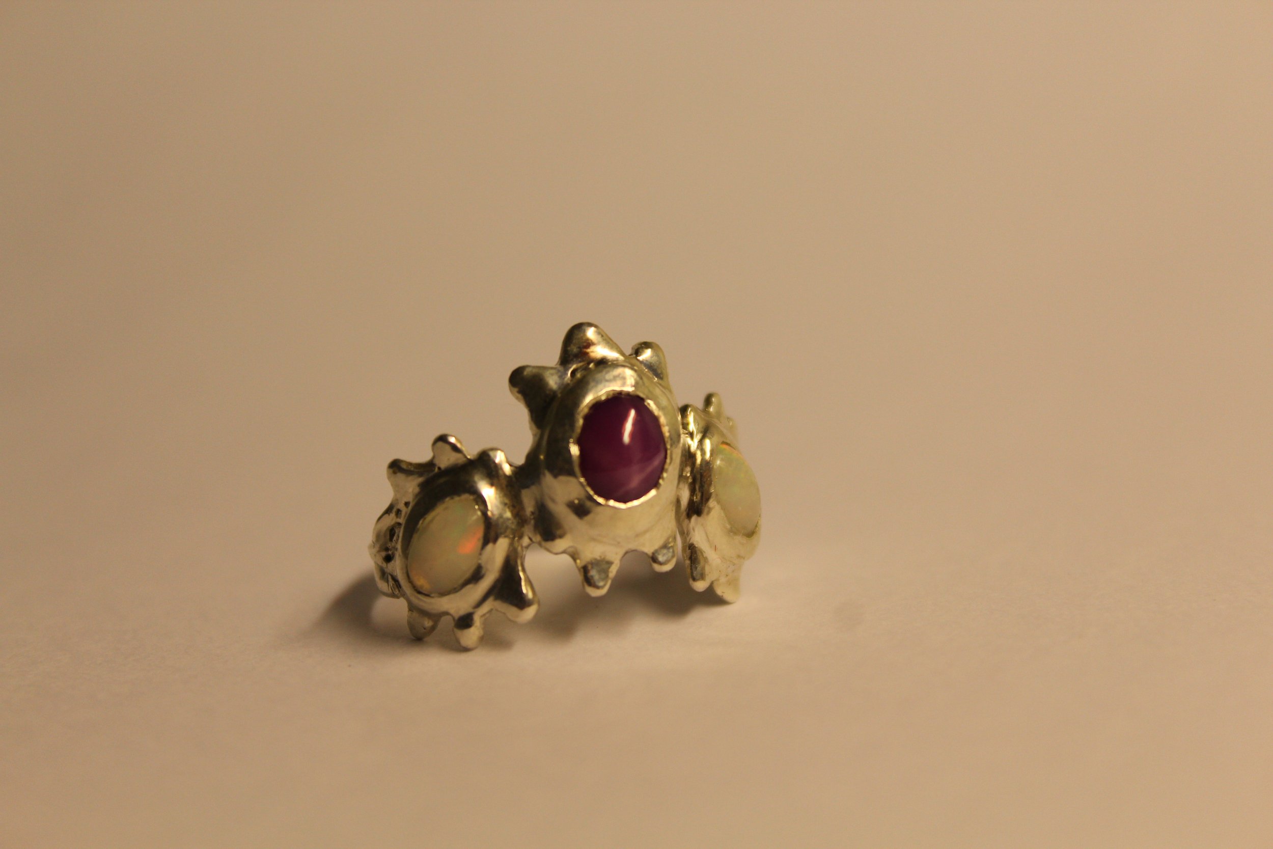 Silver ring with a large purple stone and two smaller opal-like stones on each side, on a plain surface.