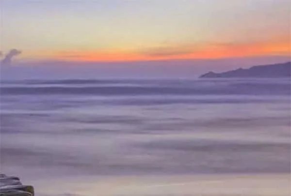 A sunset over the ocean with a distant landmass and a colorful sky.