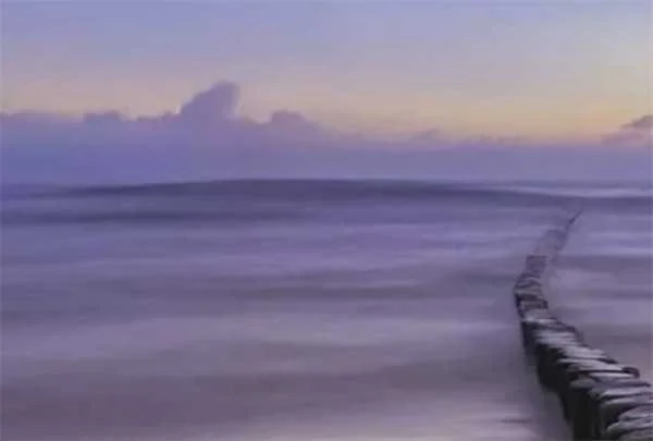 A serene beach scene during sunset with a pier extending into the water and calm waves.