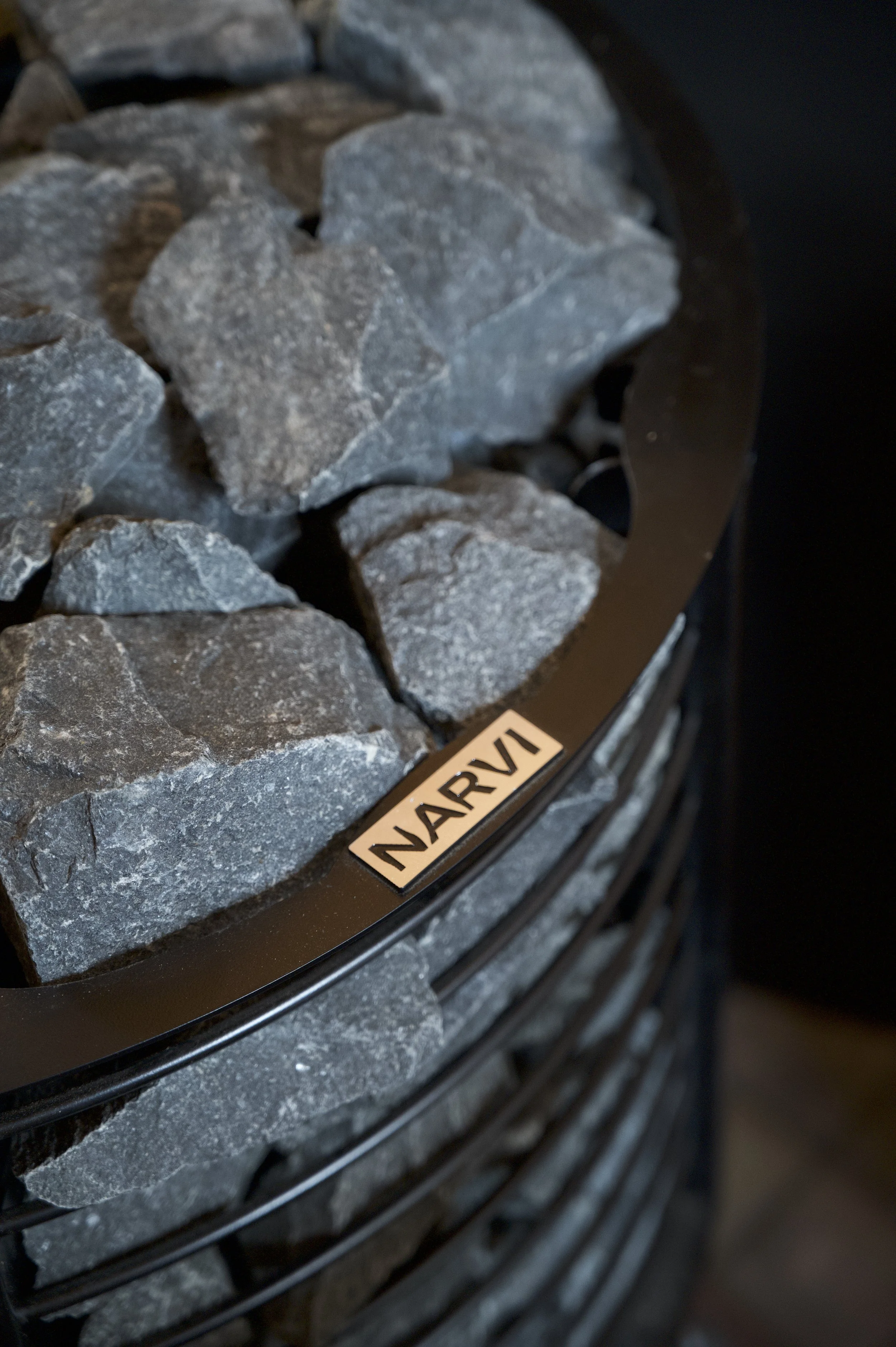 Close-up of a pile of gray rocks or stones in a black metal container with a label that says "NARVIK".