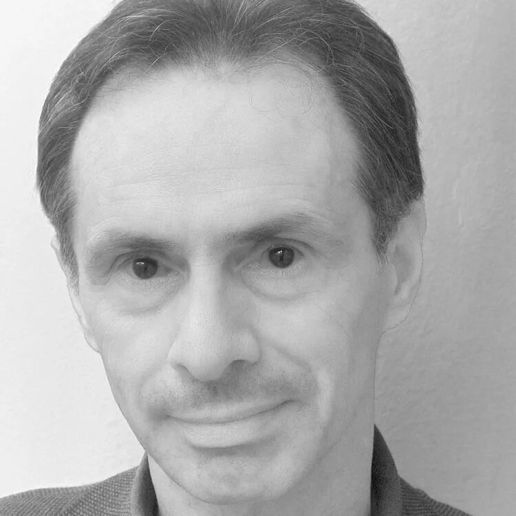 Black and white close-up photo of a middle-aged man's face with short, dark hair neatly combed, wearing a collared shirt or jacket.