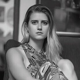 Black and white portrait of a young woman with long hair, sitting indoors with a serious expression.