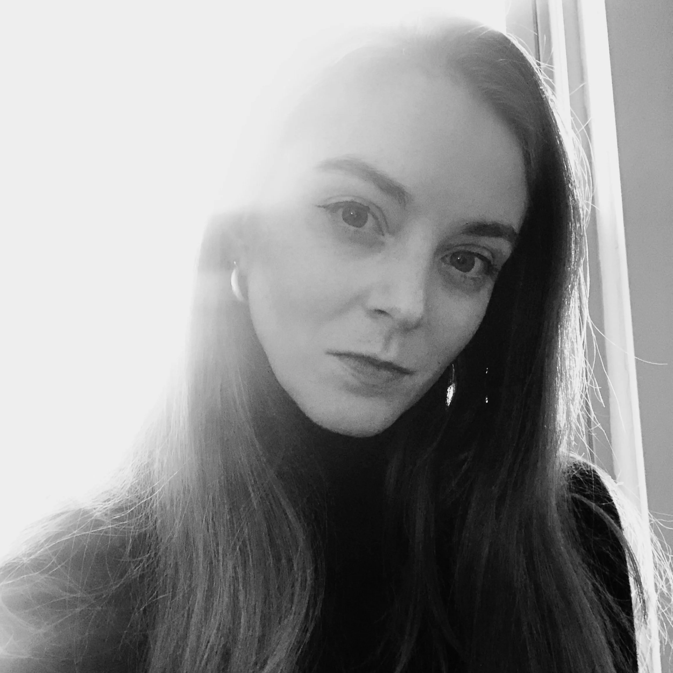 Black and white portrait of a young woman with long hair, gazing into the camera, lighting coming from behind, creating a high contrast effect.