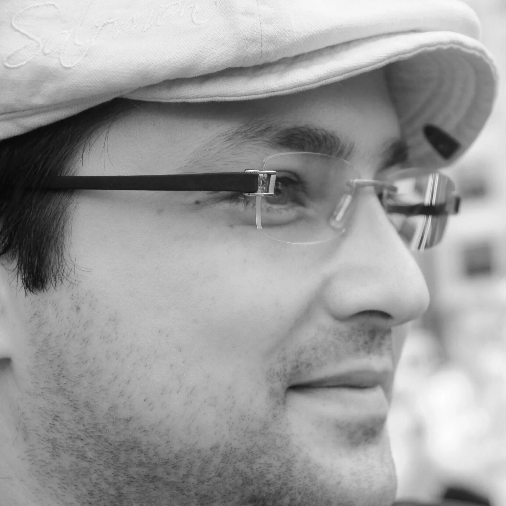 Close-up of a man wearing glasses and a hat, looking to the side in black and white.