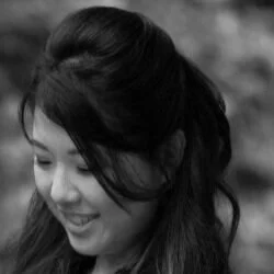 A woman smiling with her head tilted downward, hair styled in loose waves, in black and white.