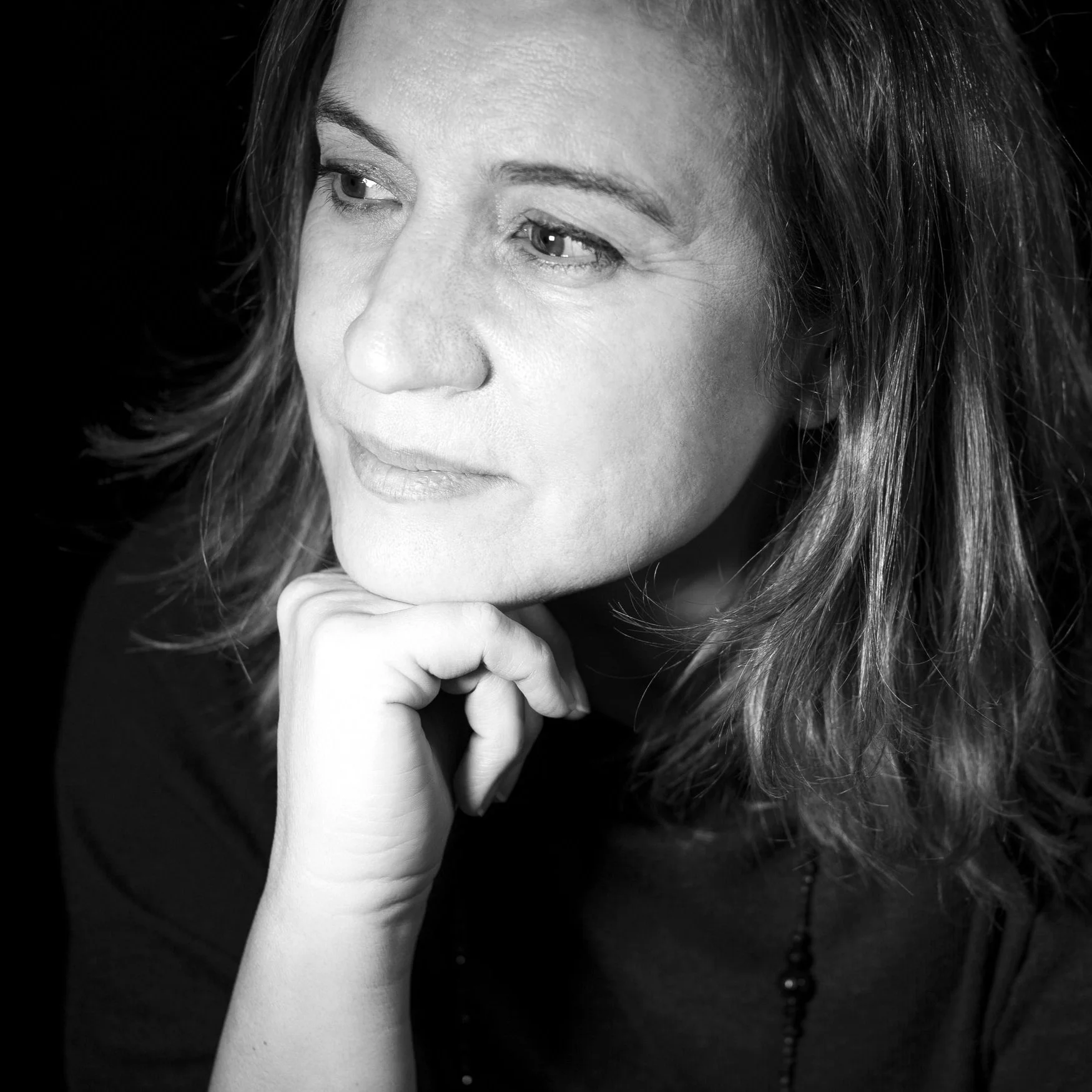 Black and white portrait of a woman with wavy hair, looking thoughtfully to the side, resting her chin on her hand.