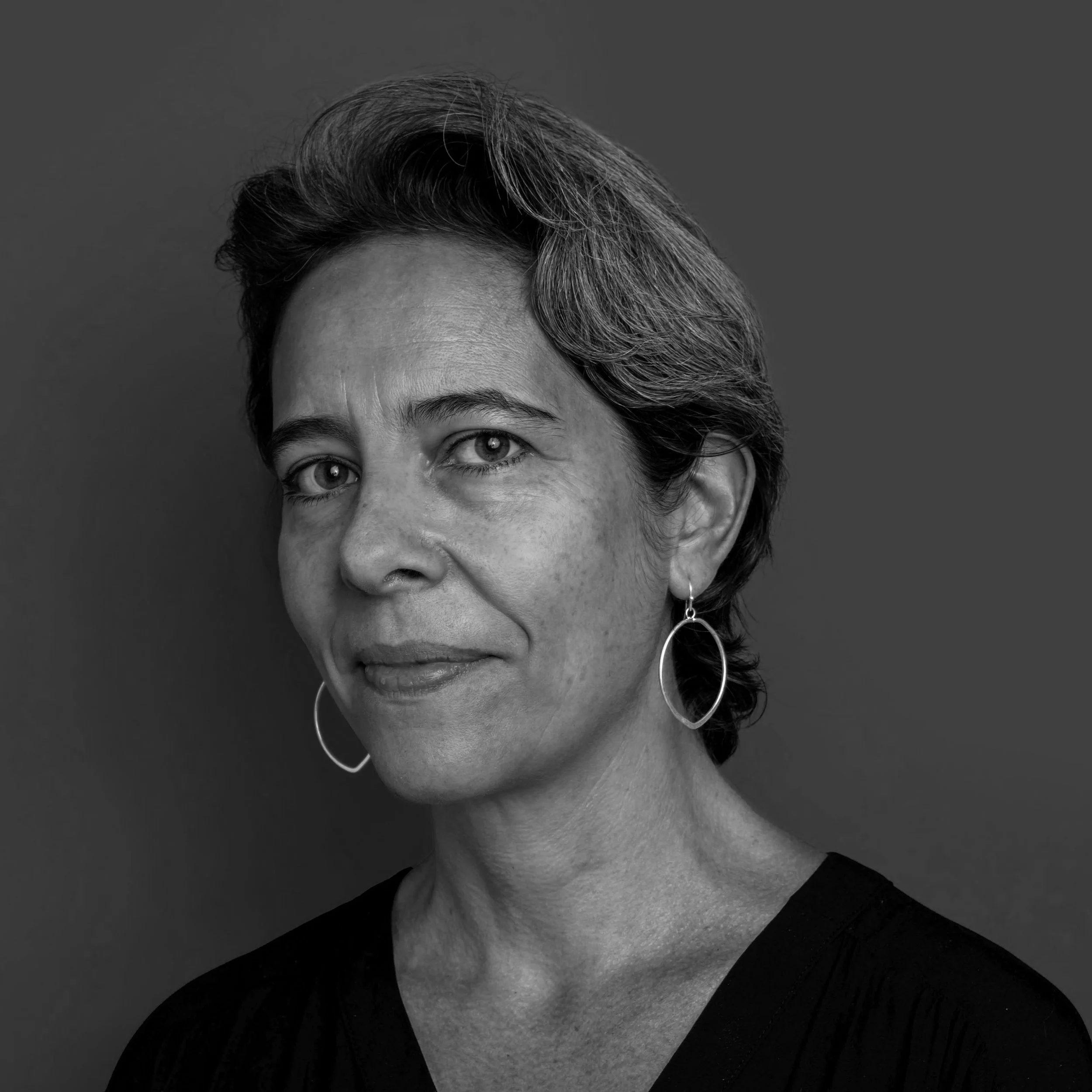 Black and white portrait of a woman with short hair, wearing hoop earrings, looking at the camera with a slight smile.