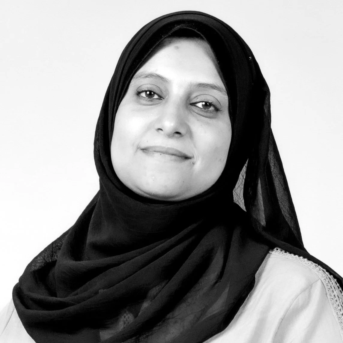 Black-and-white portrait of a woman wearing a headscarf, facing slightly to the right with a gentle smile, against a plain background.