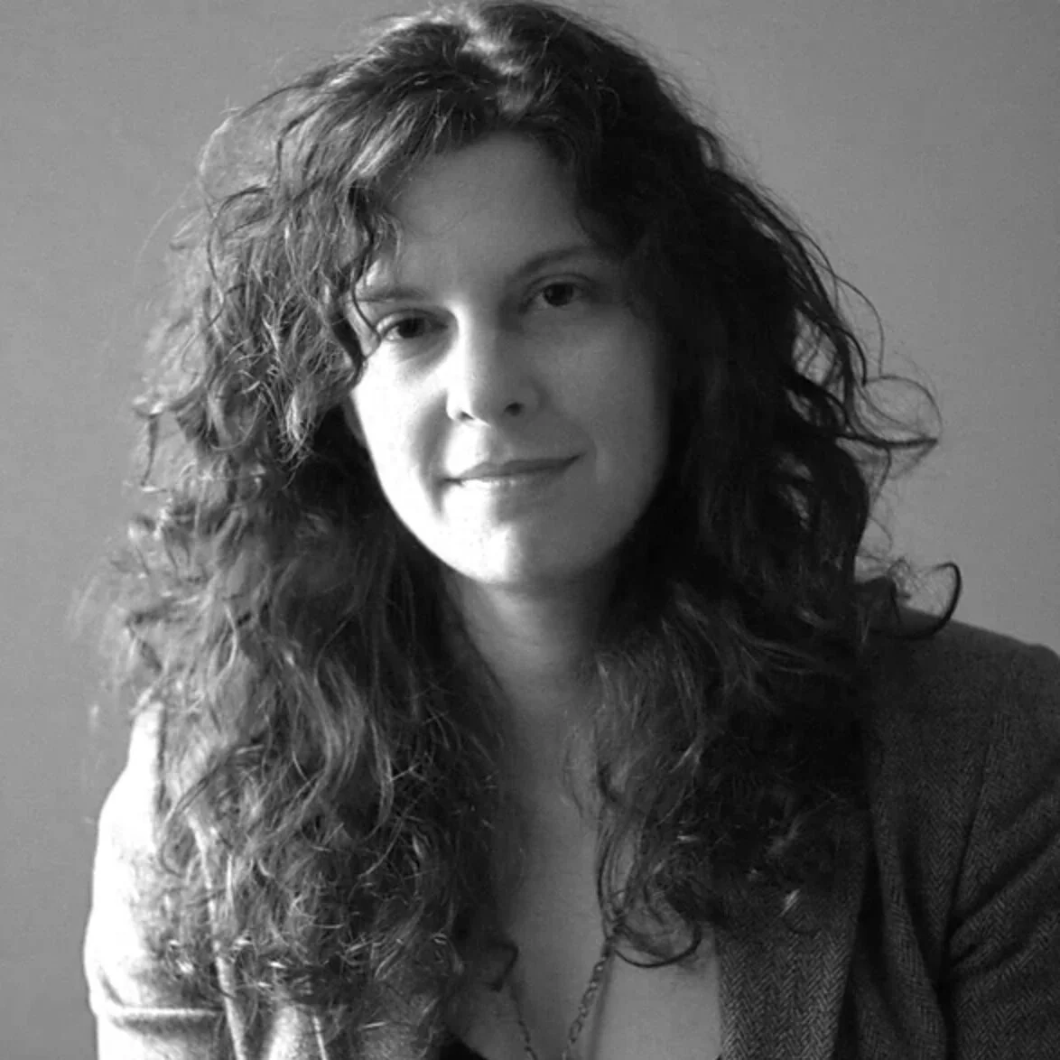 A black and white portrait of a woman with curly hair, smiling slightly, wearing a blazer.