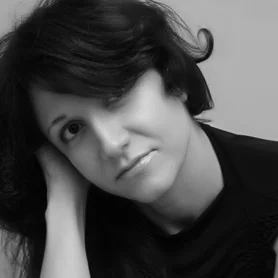 Black and white portrait of a woman with dark hair, resting her head on her hand and gazing at the camera.