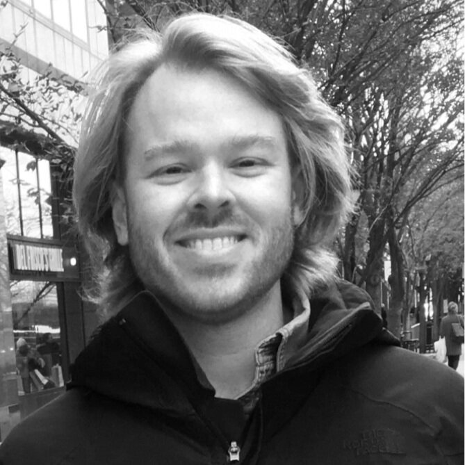 Black and white photo of a smiling young man with shoulder-length hair, wearing a jacket outdoors.