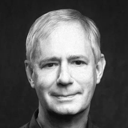 Black and white portrait of a middle-aged man with short, light-colored hair, smiling gently at the camera.