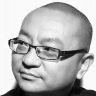 A black-and-white photo of a man with a shaved head and glasses, looking slightly to the side.