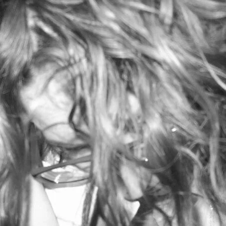 Close-up of a person with long, curly hair and glasses, slightly obscured by their hair.