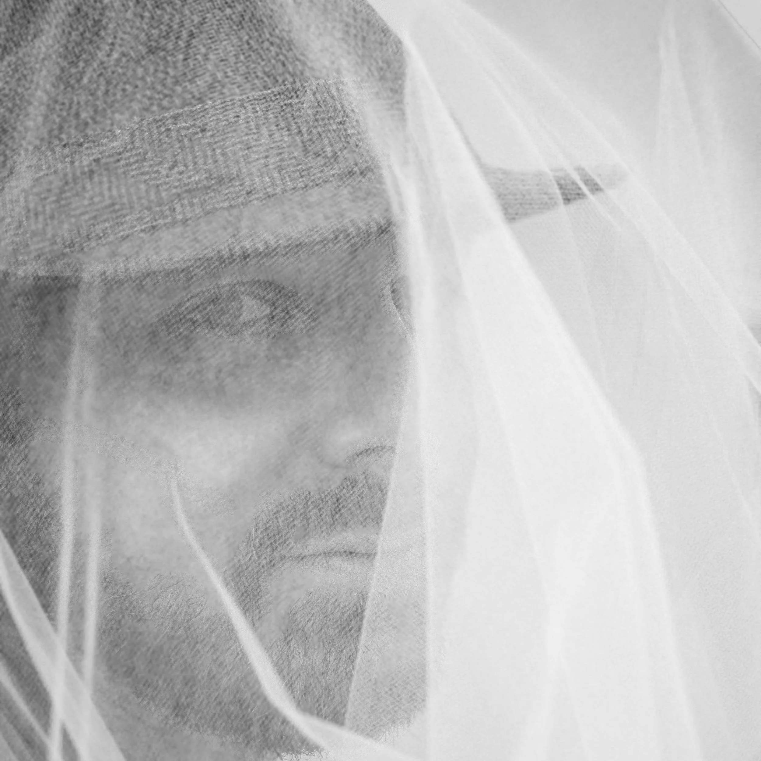 Black and white photo of a person's face partially obscured by a sheer veil or fabric.