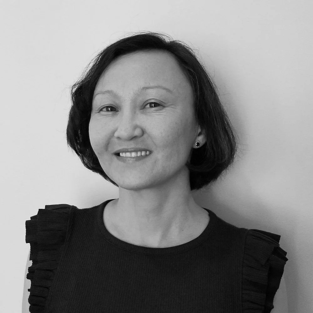 Black-and-white portrait of a woman with short dark hair, wearing a top with ruffled sleeves, smiling against a plain light background.