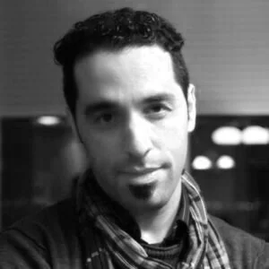 Black and white photo of a man with curly hair, wearing a striped scarf, smiling slightly.