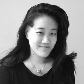 Black and white photo of a woman with long hair, smiling, wearing a dark shirt and a necklace.