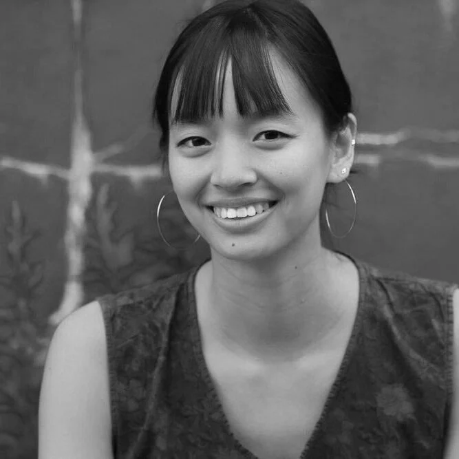Black and white photo of a young woman with short hair, large hoop earrings, and a sleeveless shirt, smiling outdoors.