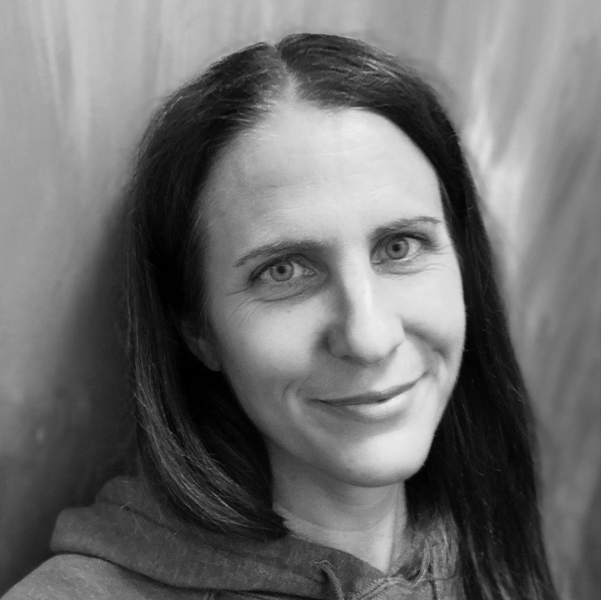 Black and white portrait of a woman with long dark hair, smiling gently, wearing a hoodie.
