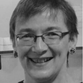 A smiling woman wearing glasses and earrings.