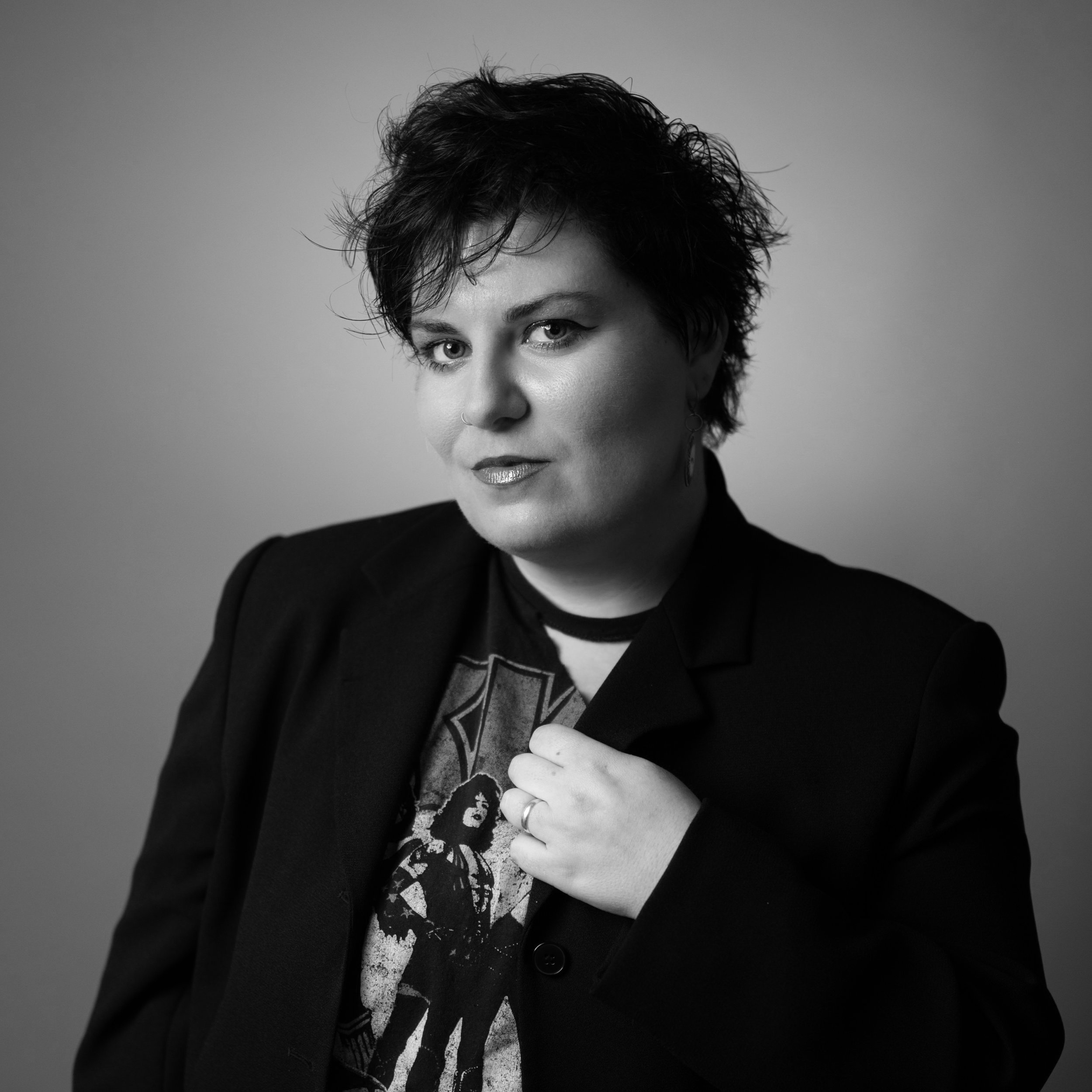 Black and white portrait of a woman with short, tousled hair, wearing a dark blazer and a graphic t-shirt, looking confidently at the camera.