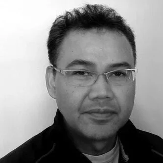 Black and white photo of a man wearing glasses and a dark jacket, looking at the camera.