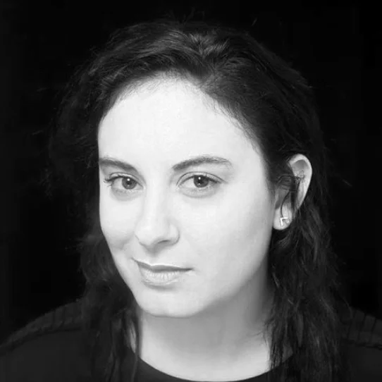 Black and white portrait of a woman with dark hair, wearing earrings, looking at the camera with a slight smile.