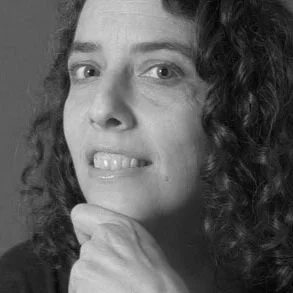 Close-up photo of a woman with curly hair looking at the camera, smiling slightly, with her hand resting on her chin in black and white.