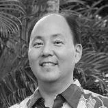 A portrait of an Asian man smiling, with a blurred natural outdoor background.