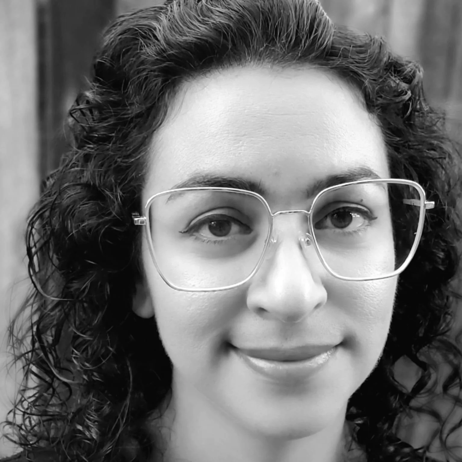 A woman with curly hair and glasses smiling at the camera, black and white photo.
