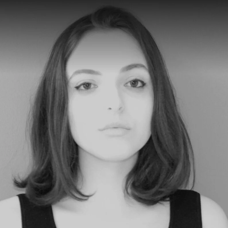 Black and white photo of a young woman with shoulder-length hair, wearing a sleeveless top, looking directly at the camera.