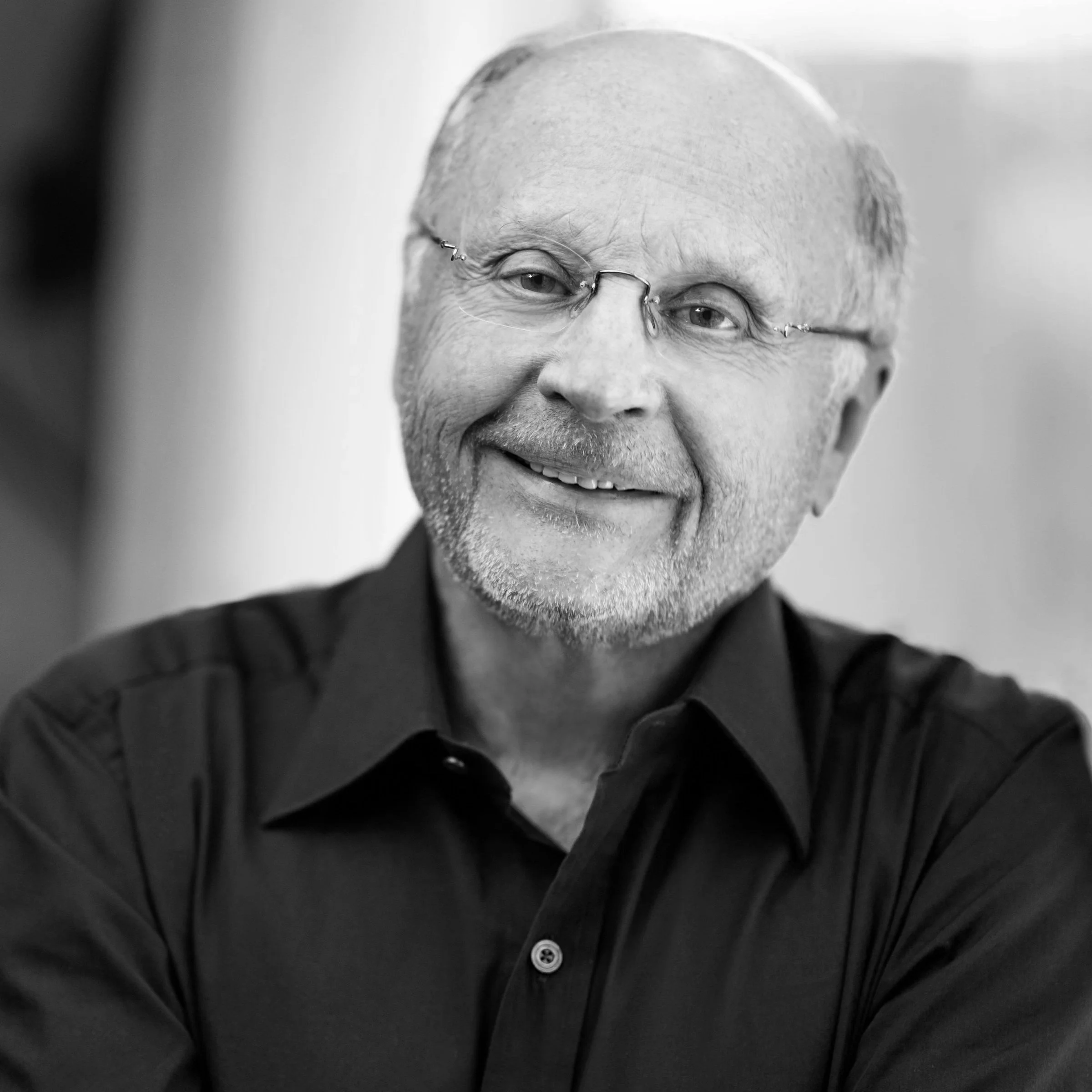 Black and white portrait of a smiling middle-aged man wearing glasses and a dark button-up shirt.