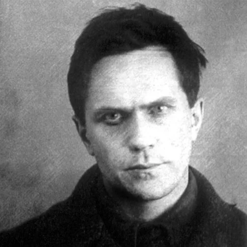 Black and white portrait of a young man with dark hair, wearing a dark shirt or jacket, with a serious expression.