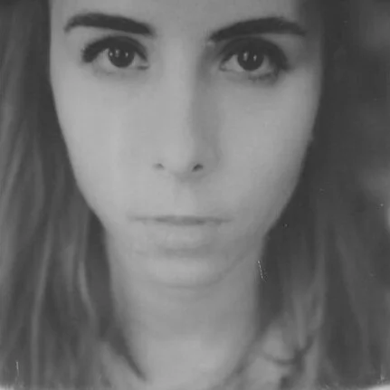 Close-up black and white portrait of a woman with straight hair, large eyes, and a neutral expression.