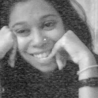 Close-up of a smiling woman with a nose piercing, resting her chin on her hand