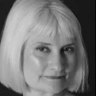 Black and white close-up of a woman with shoulder-length blonde hair, smiling slightly.