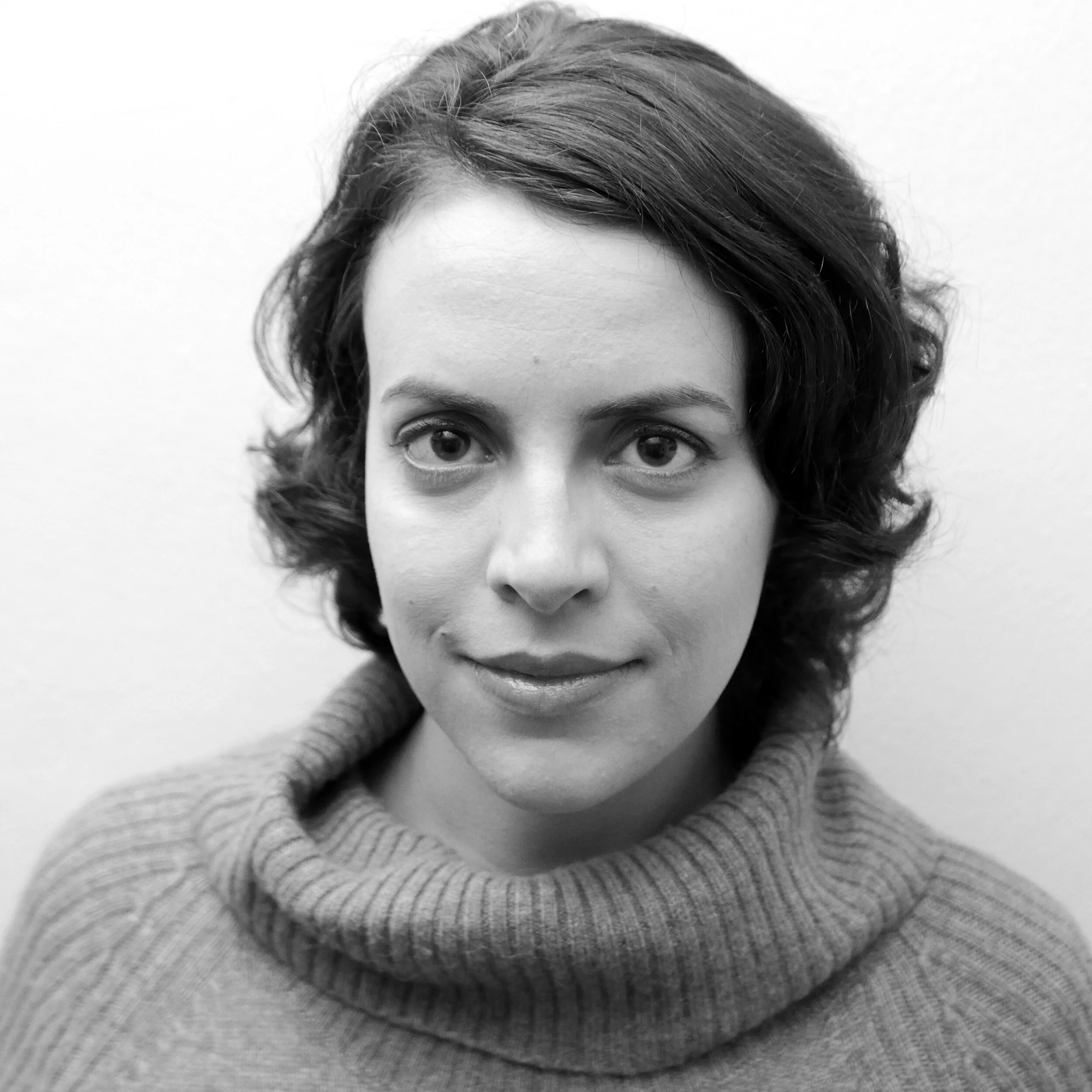 Black and white portrait of a woman with short, wavy hair wearing a turtleneck sweater, looking directly at the camera.