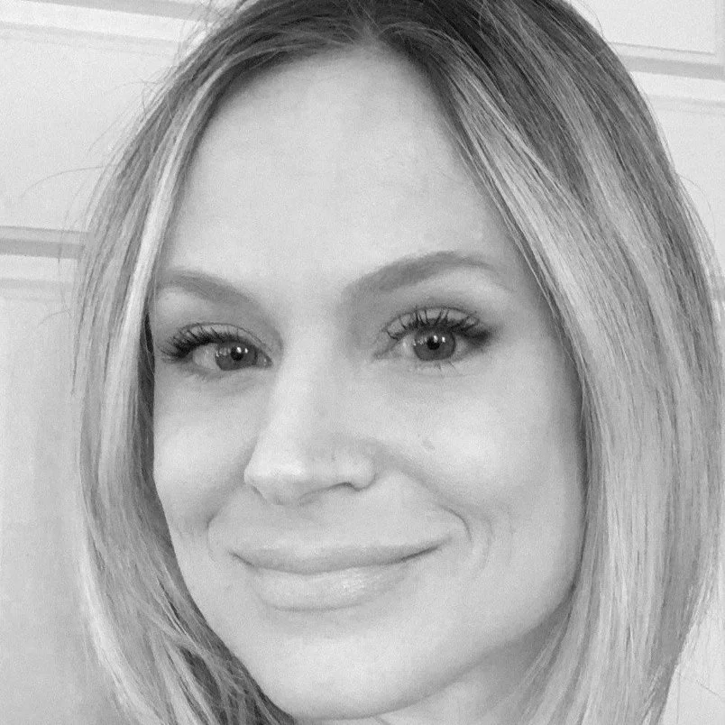 A close-up black and white photograph of a smiling woman with shoulder-length hair, light-colored eyes, and natural makeup.