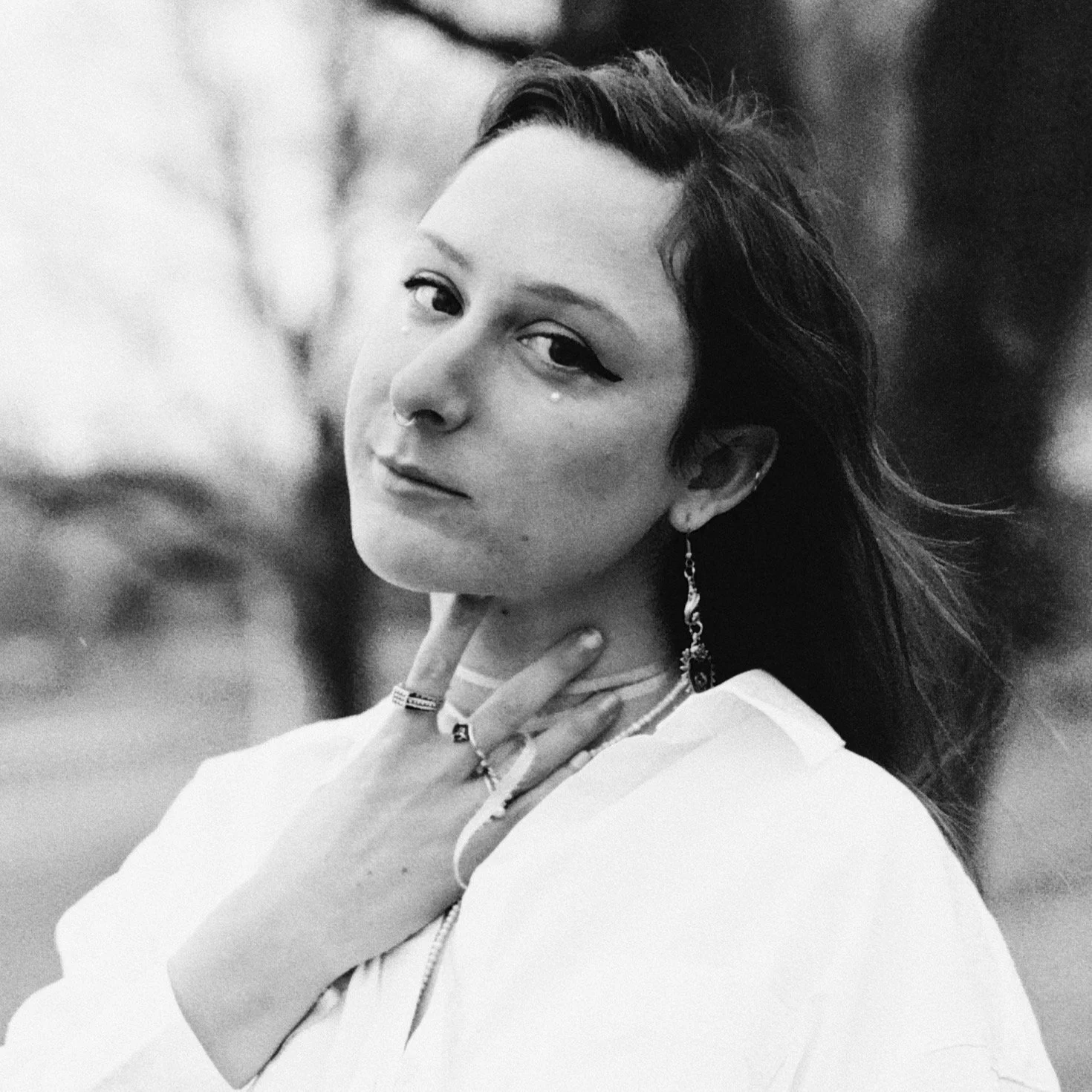 Black and white portrait of a woman with dark hair, earrings, and rings, looking at the camera outdoors.