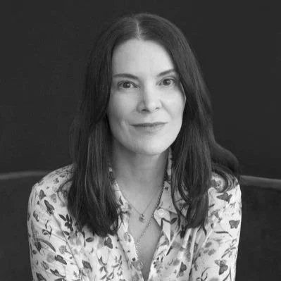 Black and white portrait of a woman with long dark hair, wearing a floral patterned blouse and smiling slightly.