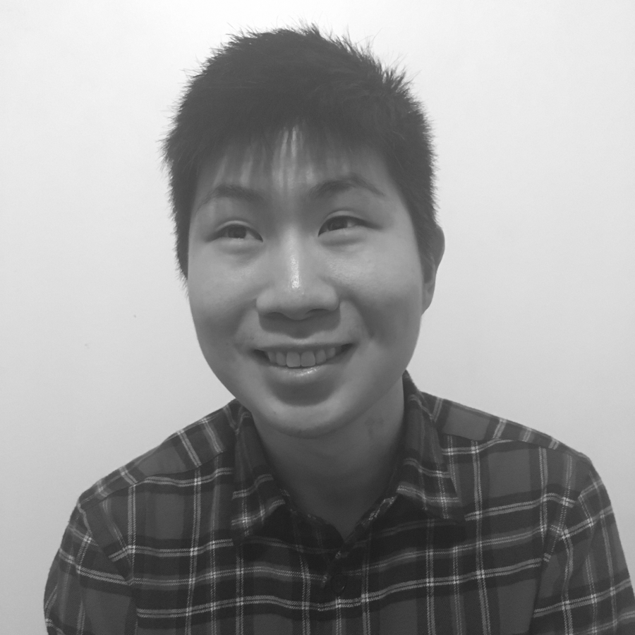 Black and white photo of a young man with short, spiky hair wearing a plaid shirt and smiling, against a plain background.