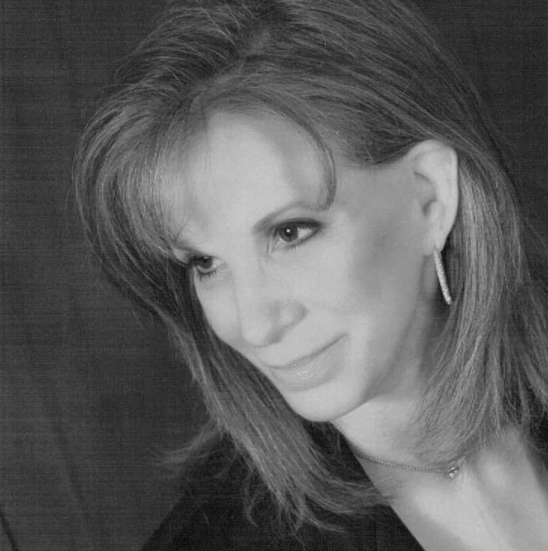 Black and white portrait of a woman with shoulder-length hair, wearing earrings and a necklace, looking to her left with a slight smile.