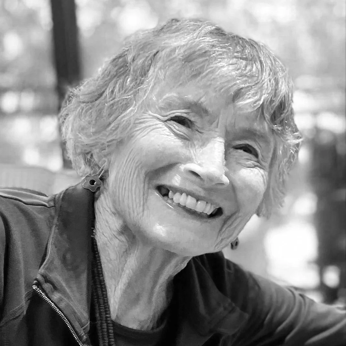 woman with curly bob, smiling at camera, in jacket and T-shirt, earrings