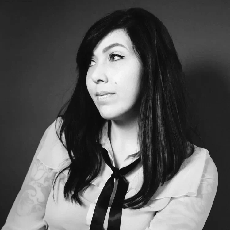 Black and white portrait of a woman with dark hair, wearing a light-colored blouse with a black ribbon tie, looking to the side.