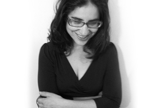 Black and white photo of a woman with dark hair and glasses smiling and looking down, wearing a black top.