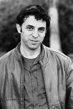 Black and white portrait of a man with curly hair wearing a jacket outdoors.