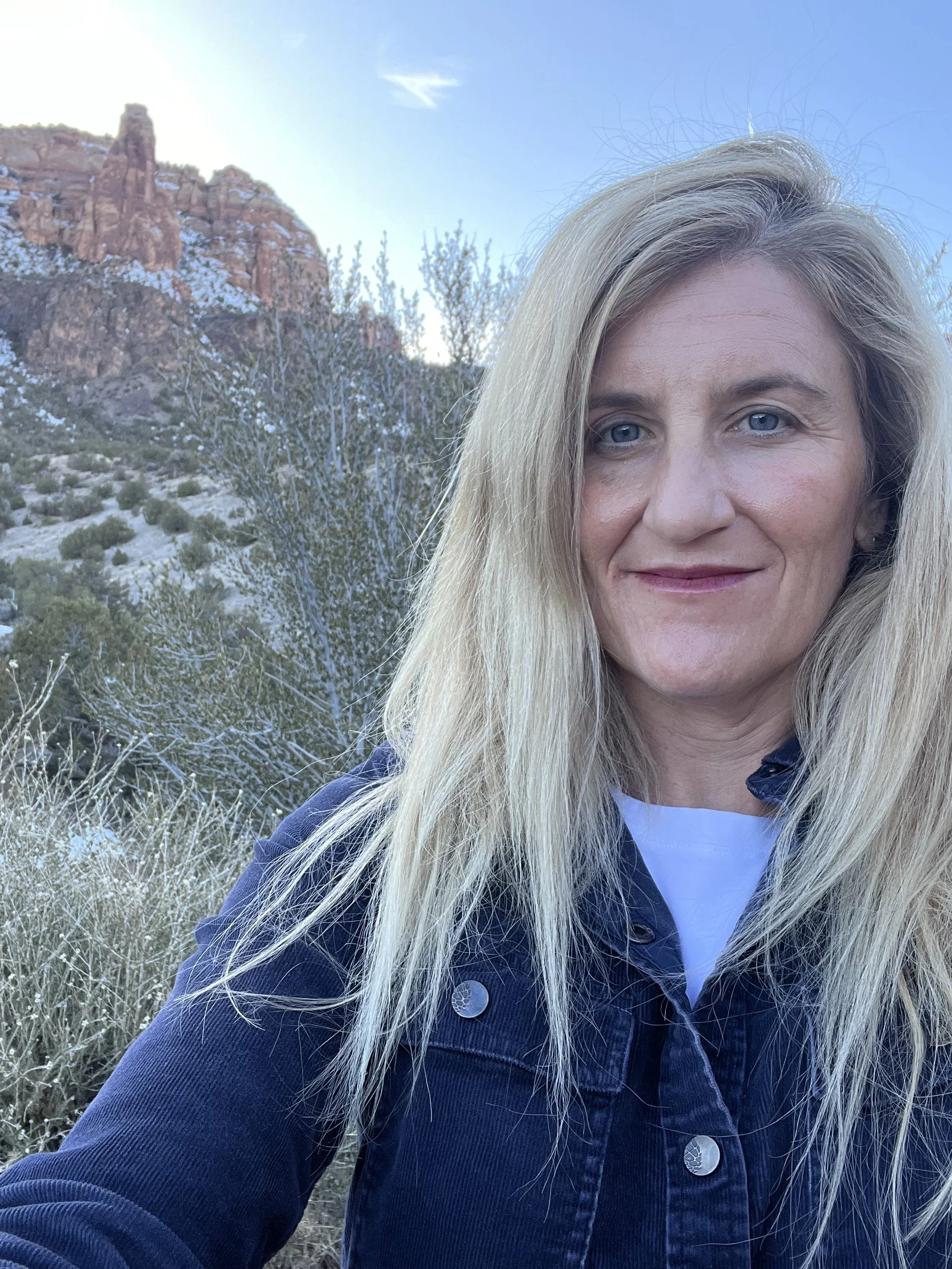 A selfie of a blonde middle-aged woman standing in front of a rocky backdrop.