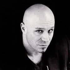 Black and white portrait of a bald man with a serious expression, looking directly at the camera.